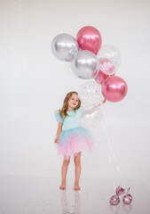 Obraz na płótnie Canvas little girl in a festive dress with a tutu skirt holds a bunch of inflatable balloons on a white background with a place for text