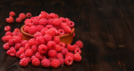 Raspberries in a clay bowl on a dark wooden table, selective focus. Close-up of ripe raspberries with copy space, idea for a banner. Ingredients for raspberry juice or desserts