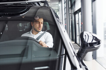 Young man in white shirt is sitting inside of a modern new automobile