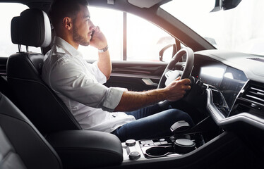 Young man in white shirt is sitting inside of a modern new automobile