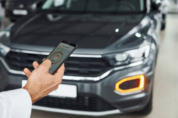 Black car. Close up view of man's hand that holds phone with labels and icons. Conception of remote control