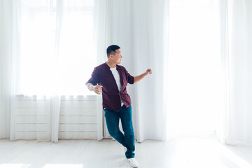 Beautiful Asian man dances to music in white room