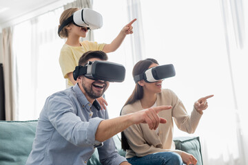 cheerful family gaming in vr headsets and pointing with fingers at home