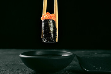 Gunkan maki sushi with salmon and spicy sauce on a black board. Japanese kitchen. Food delivery. Sticks hold sushi