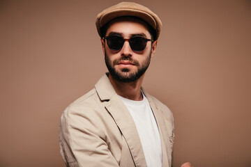 Portrait of man wearing beige jacket, cap and sunglasses on isolated background
