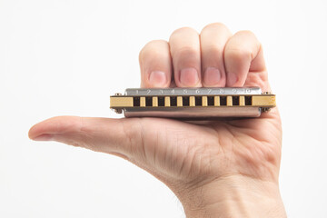 The hand holds a harmonica on a white background. Classical musical wind instrument