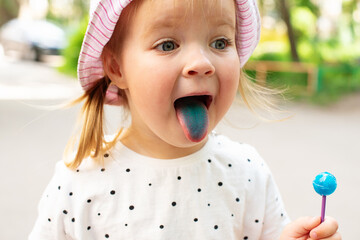 Little girl licking lollypops and showing colored blue tongue. Concept of food coloring in children's sweets, artificial food dyes, natural dyes, food coloring allergies