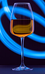 A close-up of a clean glass filled with white wine against a black background with blue streaks painted with light. Plain surface, reflections, no splashes. Restaurant glassware, serve, passion, love.