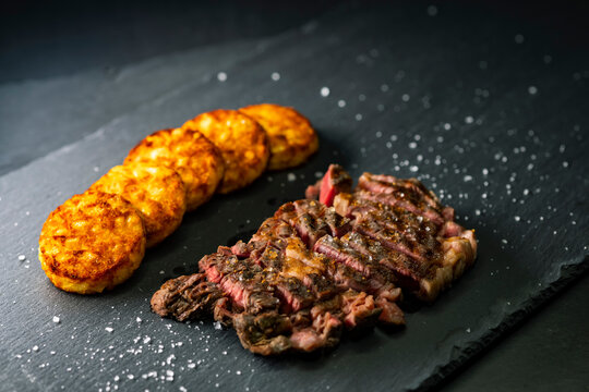 beef steak with potato patties on a dark background
