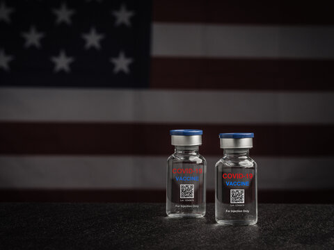 COVID-19 vaccine bottles against the background of the United States flag. Vaccine for immunization, and treatment from coronavirus infection. Close-up photo. Concept of medical and healthcare