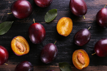 Close up image of juicy organic whole and halved plums with green leaves & visible core texture on wooden texture tabletop background, copy space. Macro shot of fruit slices. Top view, flat lay.