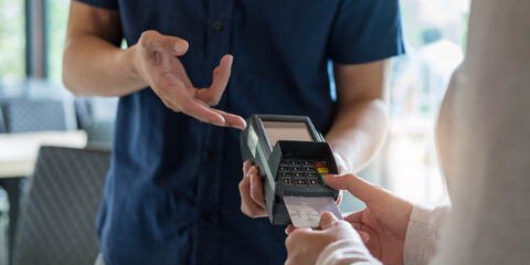 Hand of customer paying with contactless credit card with NFC technology. Bartender with a credit card reader machine at bar counter with female holding credit card. Focus on hands.