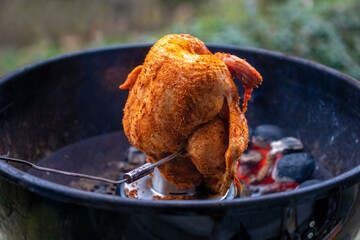 Marinated chicken on a chicken holder with thermometer on a barbecue with glowing charcoals. Close-up during a barbecue in the garden.