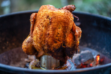Marinated chicken on a chicken holder with thermometer on a barbecue with glowing charcoals. Close-up during a barbecue in the garden.