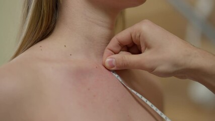 Close-up female collarbone with male hand holding tape measuring chest. Unrecognizable expert male plastic surgeon consulting young Caucasian woman on breast correction. Aesthetic surgery