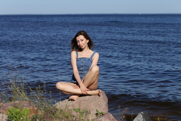 Beautiful woman in denim dress sitting on the stone in water