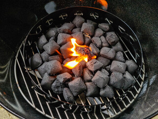 Burning barbecue lighter between charcoal briquettes on a charcoal grate in a kettle grill.
