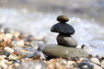 Fototapeta na wymiar Tower of pebbles on background of the sea waves. Summer vacation, balance and relax concept