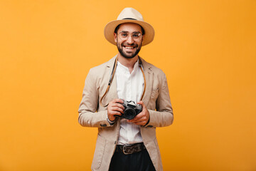 Guy in beige suit and hat posing with retro camera on orange background