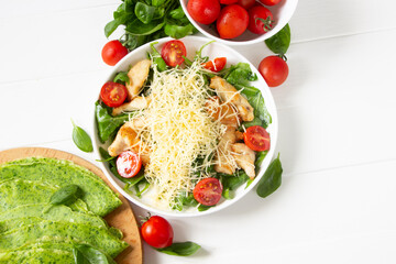 Chicken salad with cheese and tomato , basil,  spinach pancakes, spinach leaves. White wooden board