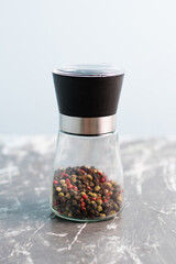 Glass pepper mill with a mixture of peppercorns on a light background, vertical format.