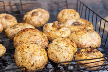 Close-up of mushrooms on barbecue grill gridiron with cook's hand