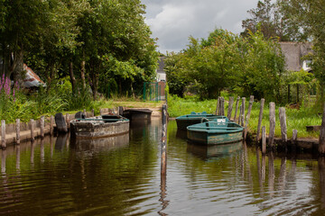 Fototapeta na wymiar Quatre barques sont attachées sur des piquets en bois dans le marais de Brière en France. Des arbres entourent le petit port.
