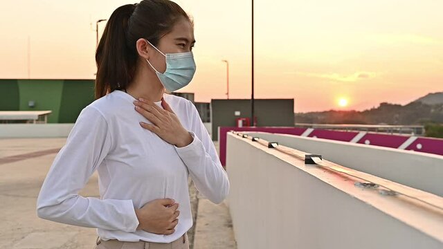 Sickness Asian woman coughing after wearing surgical mask for protect herself from bad air pollution or virus spreading and then she looking to sunset.