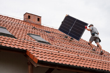 Two engineers on the house roof carry photovoltaic panel.