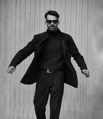 Fashion beard style business handsome male model in fashion sunglasses with serious concentrated look whirling and moving in style clothing on wall