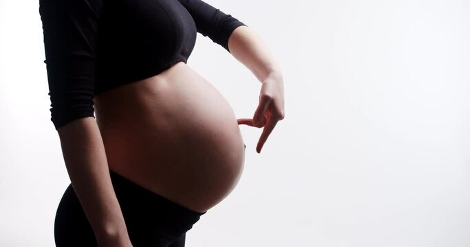 A Young cute smiling caucasian attractive beautiful fit girl walks with her tiny fingers on a pregnant belly. Happy, healthy and touching pregnancy soulful moments concept. Waiting for a newborn baby