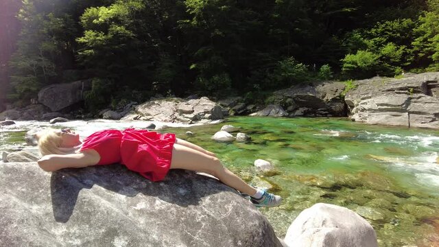 Woman relaxing sitting on the rocks of the Verzasca river. Verzasca valley by Lavertezzo town. Famous landmark for riverside leisure and high diving in Ticino, Switzerland.