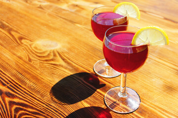 two glasses with red summer cocktails with lemon slices on a wooden background