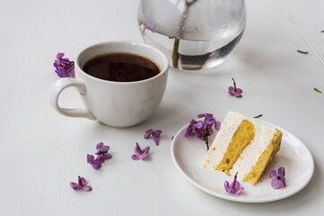 Cup of coffee and cake horns fromstill life with a bouquet of lilacs on a white table, a cup of coffee, a plate with a piece of cake. international Women's Day, March 8