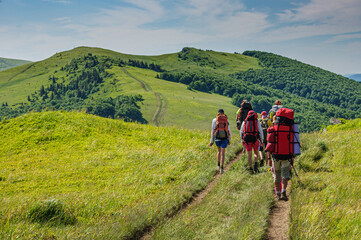 Fototapeta premium A group of tourists with large backpacks is walking along the beautiful water-producing ridge in the Carpathians. Ukraine