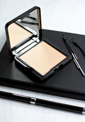 Cosmetic face powder in black square container and notebook pen earrings on wooden table