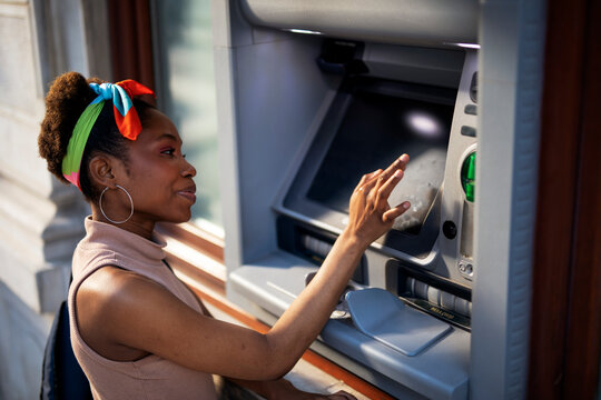 Beautiful african women using ATM machine. Attractive young woman withdrawing money from credit card at ATM..