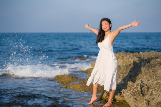 summer lifestyle portrait of young beautiful and happy Asian woman at the beach - Attractive Korean girl by the sea enjoying holidays trip on rock cliff with ocean view