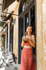 Beautiful stylish hipster young woman laughing, having take away cold coffee in outdoor summer cafe 