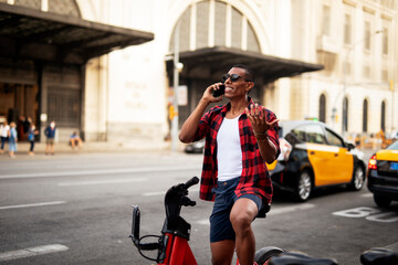 Portrait of handsome african man using electric bike in the city. Happy young man using the phone...