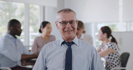 Smiling senior executive looking at camera with creative team brainstorming on background