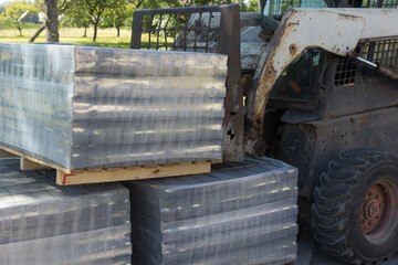 A small tractor lifts a pallet with concrete bricks. Street reconstruction.