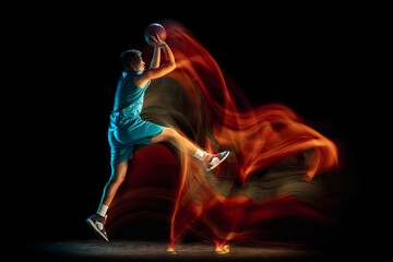 Young caucasian male basketball player playing basketball isolated over dark studio background in mixed light. Concept of healthy lifestyle, professional sport, hobby.