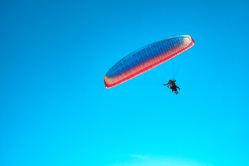 Doubles paragliding against a clear blue sky. A multi-colored papaplan flies in the clear sky closeup.