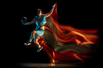 Obraz na płótnie Canvas Young caucasian male basketball player playing basketball isolated over dark studio background in mixed light. Concept of healthy lifestyle, professional sport, hobby.