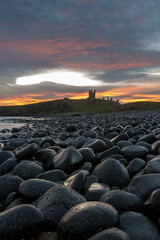 Fototapeta na wymiar The most beautiful sunrise at Dunstanburgh Castle with the famous slippery black boulders in Northumberland, as the sky erupted with colour