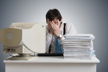 Funny man is covering face and looking on pile of documents on desk.