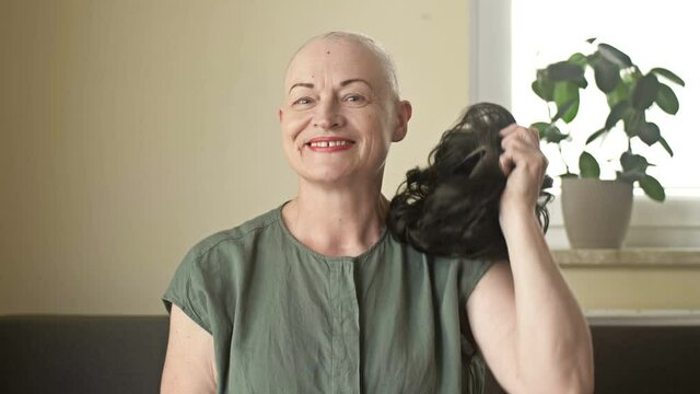 Portrait of a positive woman suffering from cancer. A woman without embarrassment takes off her wig from her bald spot after chemotherapy.