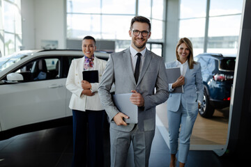 Sales team in dealership, three beautiful consultants or managers in elegant suit looking at camera.