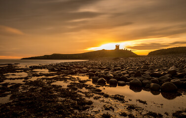 The most beautiful sunrise at Dunstanburgh Castle with the famous slippery black boulders in Northumberland, as the sky erupted with colour